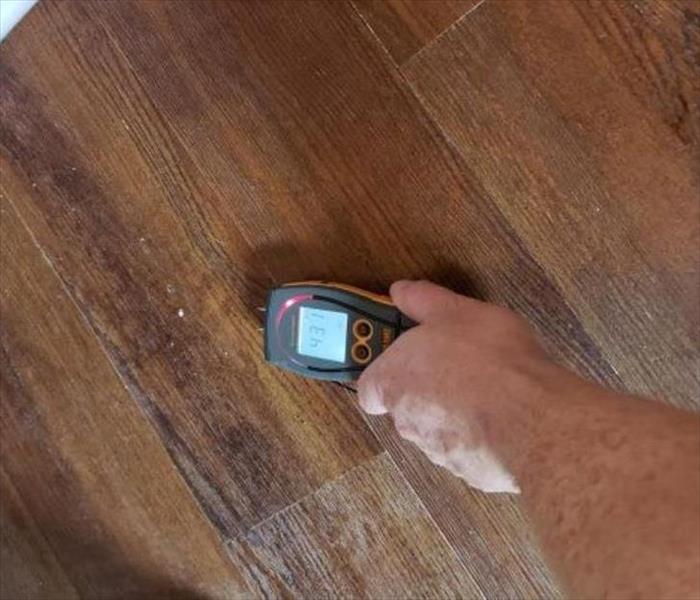 A moisture meter with a high moisture reading on a wood floor.
