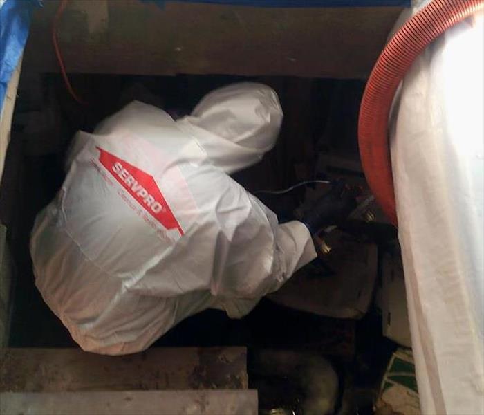 An employee in a tyvex suit cleaning in a crawl space.