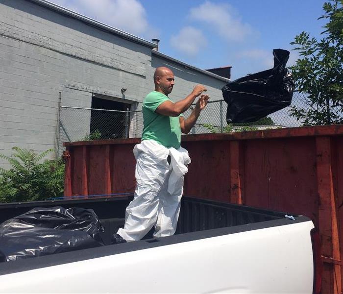 A SERVPRO employee unloading garbage into the dumpster from the bed of a truck.